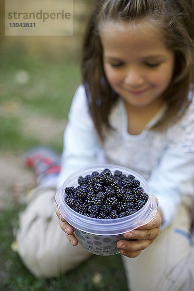 Lächelndes Mädchen hält Schüssel mit Brombeeren im Hof