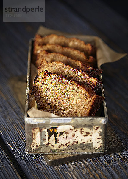 Nahaufnahme eines in Scheiben geschnittenen Bananenbrotlaibs in einem Behälter auf dem Tisch