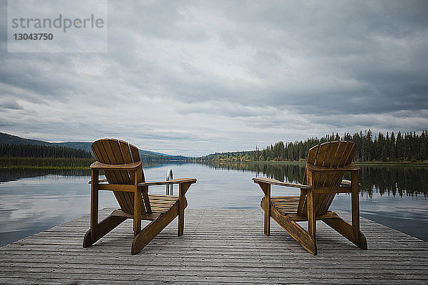 Holzstühle auf dem Pier über dem See gegen bewölkten Himmel