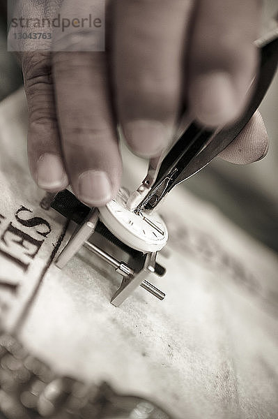 Abgetrennte Hand eines Mannes  der eine Uhr auf einem Tisch in einer Werkstatt repariert
