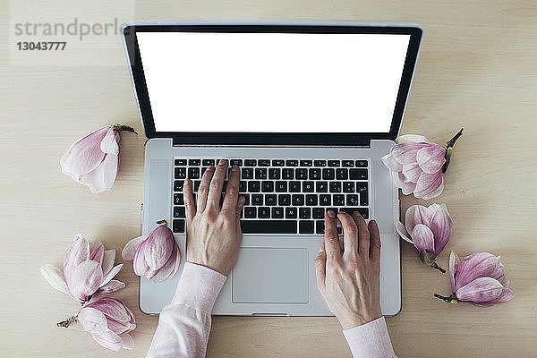 Abgehackte Hände einer Frau bei der Benutzung eines Laptops von Magnolien auf einem Holztisch