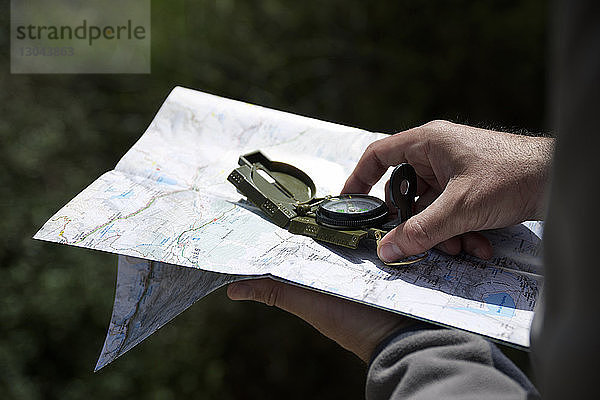 Abgehackte Hände eines Wanderers mit Navigationskompass und Karte im Wald