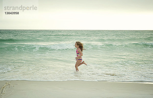 Seitenansicht eines Mädchens  das am Strand gegen den Himmel läuft