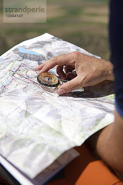 Beschnittene Hände eines Wanderers mit Navigationskompass und Karte