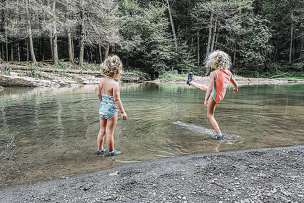 Rückansicht eines Mädchens  das seine Schwester im See stehend beim Wassertreten beobachtet