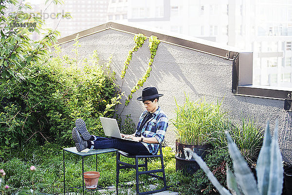 Mann benutzt Laptop  während er mit den Füßen auf dem Tisch auf der Terrasse sitzt