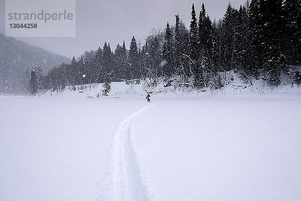Fernsicht einer Frau  die bei Schneefall auf einem schneebedeckten Feld läuft