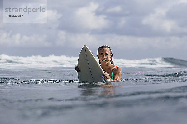 Porträt einer Frau  die ein Surfbrett im Meer gegen den Himmel hält