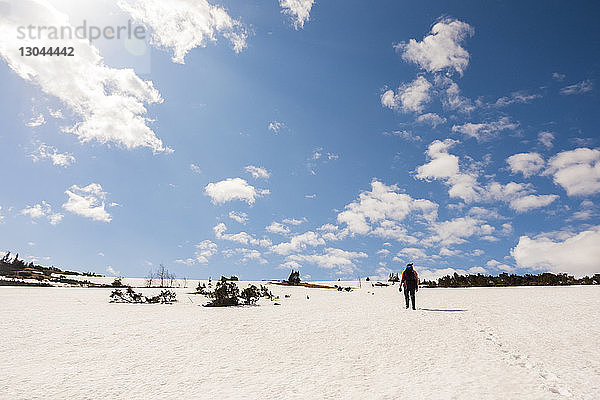 Rückansicht eines Wanderers  der auf einem schneebedeckten Feld vor bewölktem Himmel steht