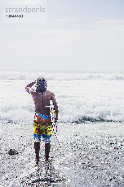 Rückansicht eines männlichen Surfer  der ein Surfbrett trägt  während er am Ufer steht