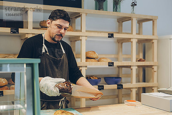Bäckereibesitzer verpackt Brot in Papiertüte  während er am Tresen steht