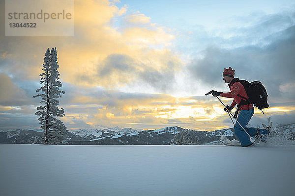 Seitenansicht eines männlichen Wanderers  der bei Sonnenuntergang auf einem verschneiten Feld Ski fährt