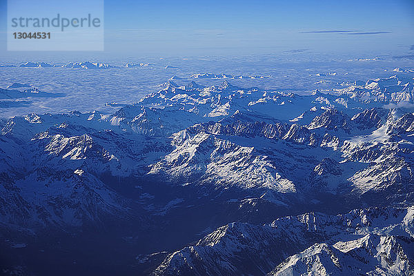 Luftaufnahme von schneebedeckten Bergen vor blauem Himmel