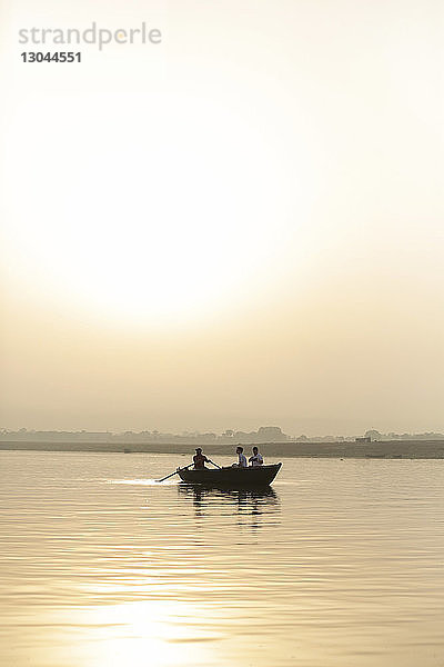 Menschen  die bei Sonnenuntergang im Boot gegen den Himmel fahren