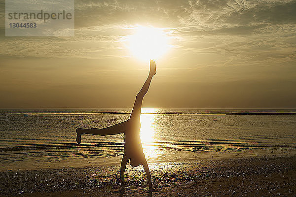 Silhouettenmädchen macht Handstand am Strand gegen den Himmel bei Sonnenuntergang