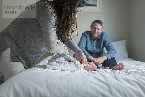 Seitenansicht der Mutter  die das Neugeborene mit einer Decke umwickelt  während der Vater im Hintergrund steht