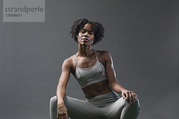 Porträt einer selbstbewussten Frau in Sportkleidung  die im Fitnessstudio an der Wand sitzt