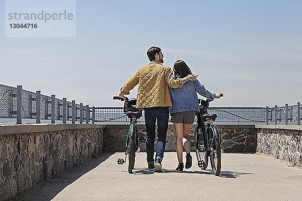 Rückansicht eines Paares mit Fahrrädern beim Gehen am Beobachtungspunkt vor klarem Himmel