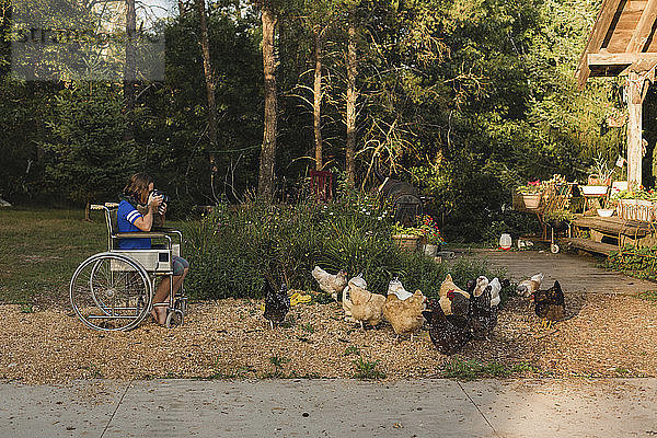 Mädchen fotografiert Hühner im Rollstuhl sitzend auf einem Bauernhof