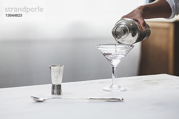 Ausgeschnittenes Bild einer Frau  die mit der Hand Alkohol in ein Martini-Glas gießt
