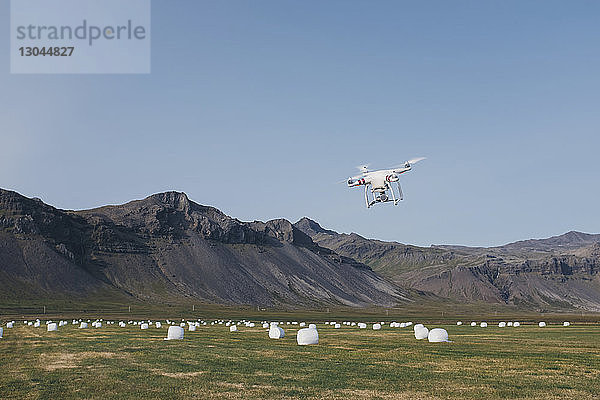 Drohne fliegt über Baumwollballen auf Feld gegen Berge und klaren Himmel