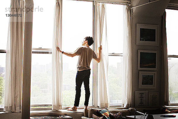 Rückansicht eines nachdenklichen Mannes  der zu Hause auf dem Fensterbrett steht