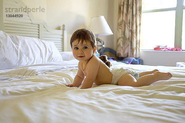 Porträt eines süßen hemdlosen Kleinkindes  das zu Hause auf dem Bett liegt
