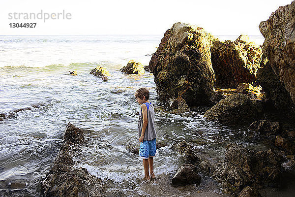 Seitenansicht eines Jungen  der am Laguna Beach gegen Felsen steht