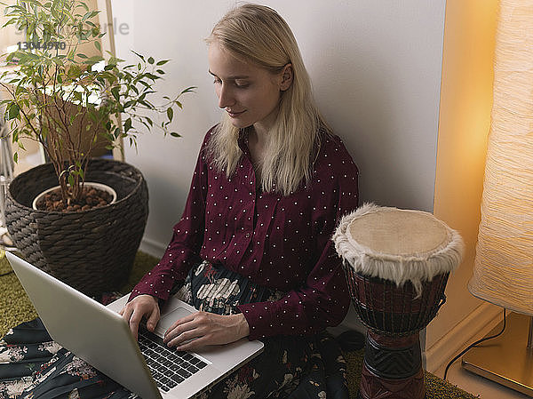 Hochwinkelansicht einer Frau  die einen Laptop-Computer benutzt  während sie zu Hause an der Wand sitzt