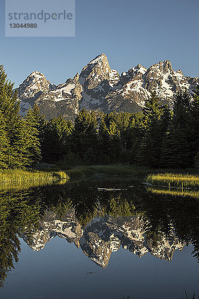 Schneebedeckter Berg vor klarem Himmel spiegelt sich auf ruhigem See im Grand-Teton-Nationalpark