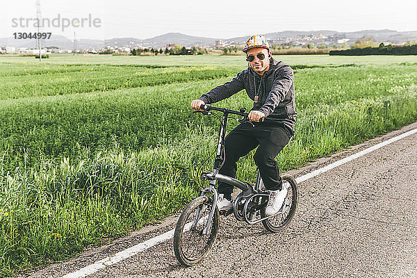 Porträt eines Fahrrad fahrenden Mannes auf Straße durch Bauernhof gegen Himmel