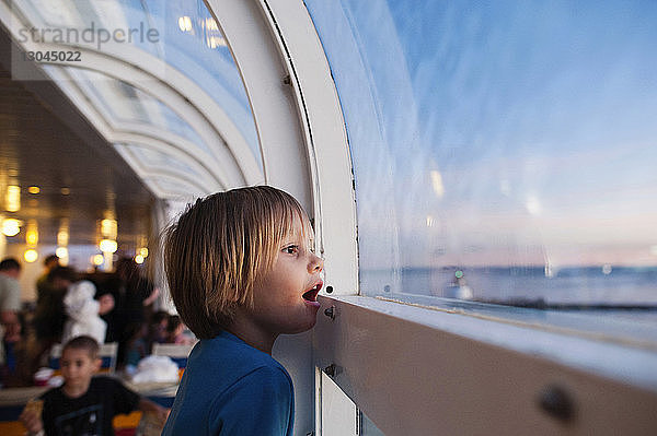 Seitenansicht eines Mädchens  das durch ein Fenster schaut  während es auf einem Kreuzfahrtschiff reist