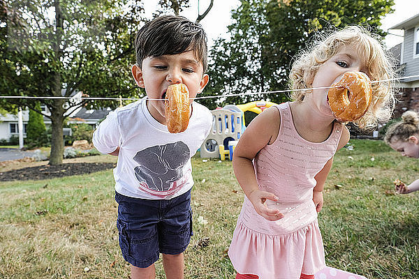 Geschwister essen während der Feier im Hof an einem Seil hängende Donuts