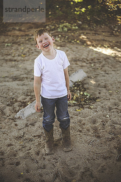 Glücklicher Junge in voller Länge auf Sand im Wald stehend