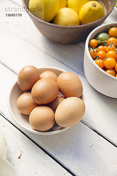 Hochwinkelansicht von Eiern mit Zitronen und Kirschtomaten in Schalen auf dem Tisch