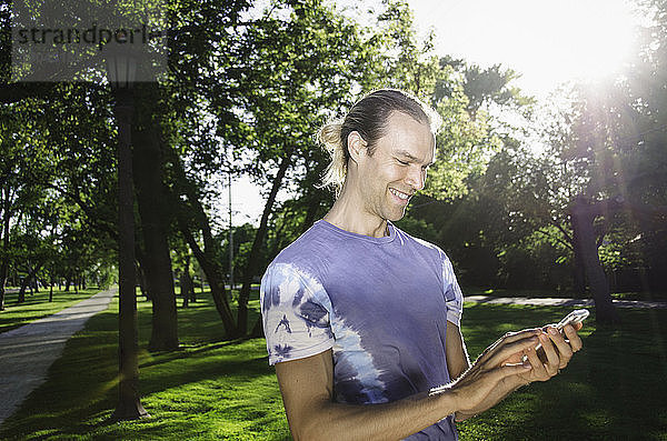 Glücklicher Mann benutzt Mobiltelefon  während er im Park steht