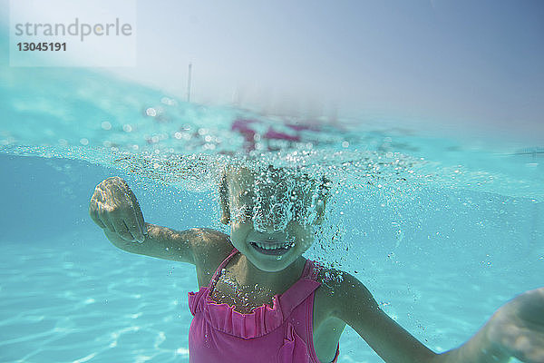 Glückliches Mädchen schwimmt unter Wasser im Pool gegen den Himmel