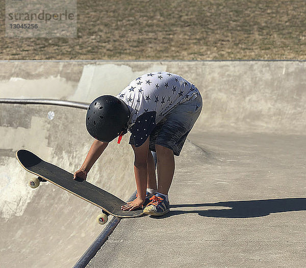 Junge in voller Länge beim Einstellen des Skateboards auf der Sportrampe auf dem Spielplatz während eines sonnigen Tages