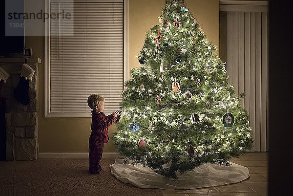 Seitenansicht eines Jungen  der zu Hause am beleuchteten Weihnachtsbaum steht