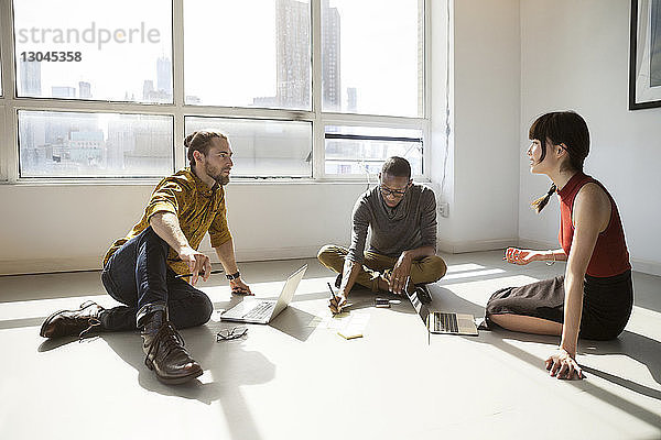 Geschäftsleute diskutieren  während sie im Kreativbüro am Boden sitzen
