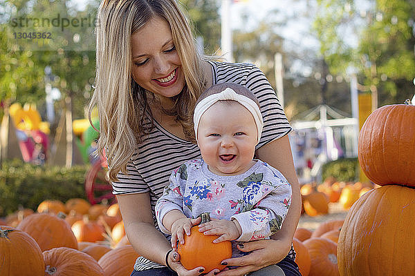 Porträt eines glücklichen Mädchens mit Kürbis in der Hand  das an Halloween mit seiner Mutter im Hof sitzt