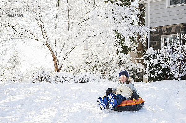 Glückliches Mädchen sitzt im Winter auf einem aufblasbaren Ring im Hinterhof