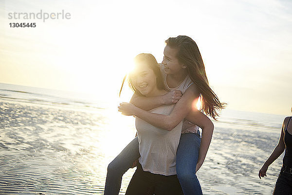 Glückliche Teenagerin mit Huckepack-Freundin am Strand