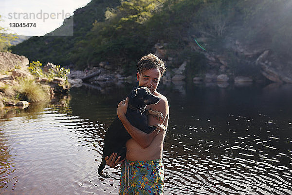 Mann ohne Hemd mit Hund steht im See am Berg