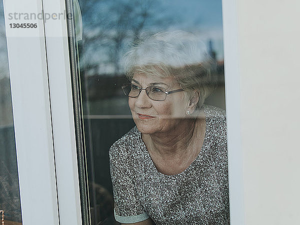 Hochwinkelansicht einer nachdenklichen Frau  die durch ein Fenster schaut