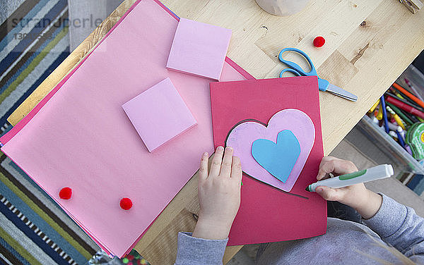 Mittendrin ein Mädchen  das zu Hause eine Valentinskarte bastelt