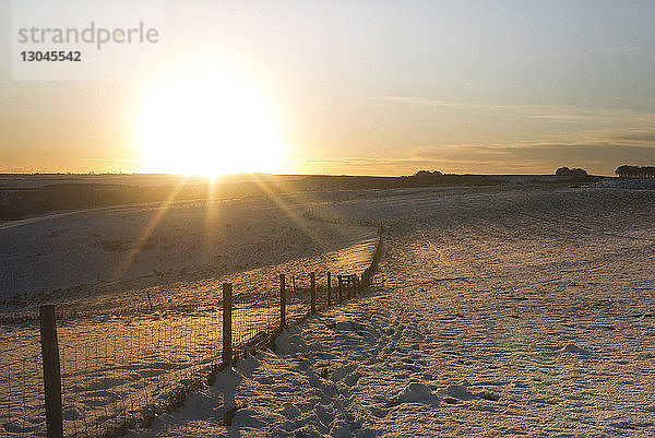 Zaun auf schneebedecktem Feld gegen den Himmel bei Sonnenuntergang