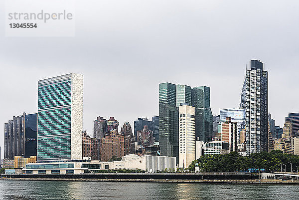 Moderne Gebäude am East River vor bewölktem Himmel in der Stadt