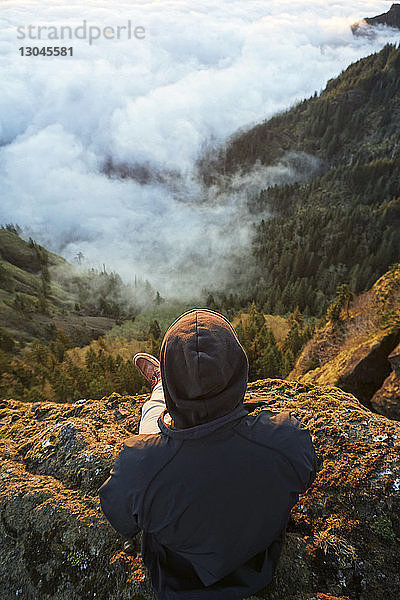 Hochwinkelansicht eines Wanderers  der auf dem Gipfel eines Berges sitzt und auf die Aussicht schaut