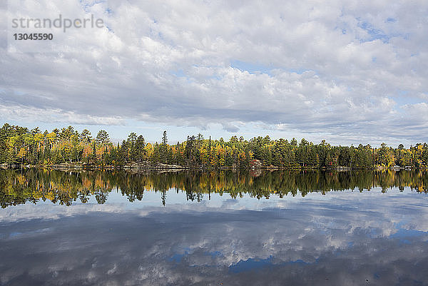 Landschaftliche Ansicht von Bäumen und bewölktem Himmel  die sich im Herbst auf dem ruhigen See spiegeln